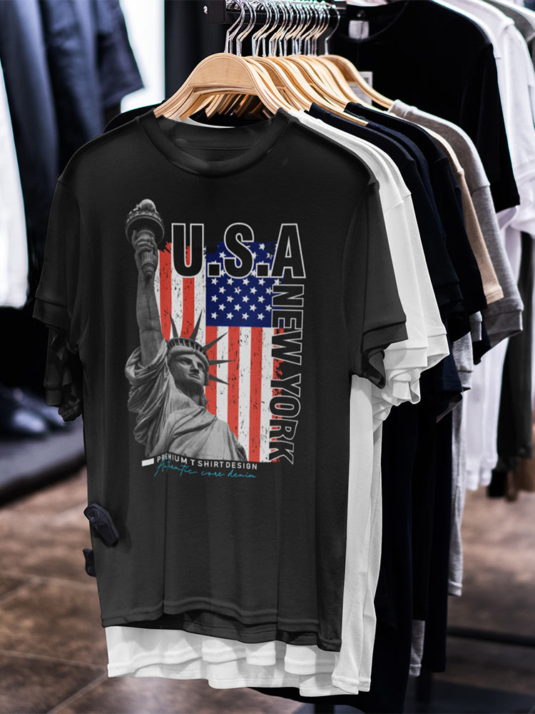 A black T-shirt with a graphic of the Statue of Liberty and the text "USA NEW YORK" displayed on a clothing rack among other shirts.