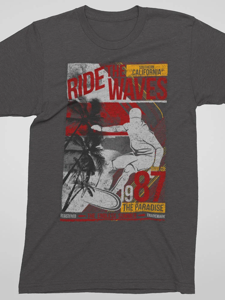 This is a gray t-shirt with a vintage-inspired surf graphic. It includes text, palm trees, and a silhouette of a surfer riding a wave.