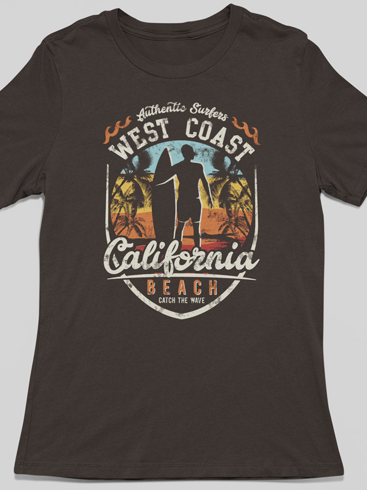 This image shows a black t-shirt with a colorful graphic depicting a person surfing, palm trees, sunset, and text that reads "West Coast California Beach."