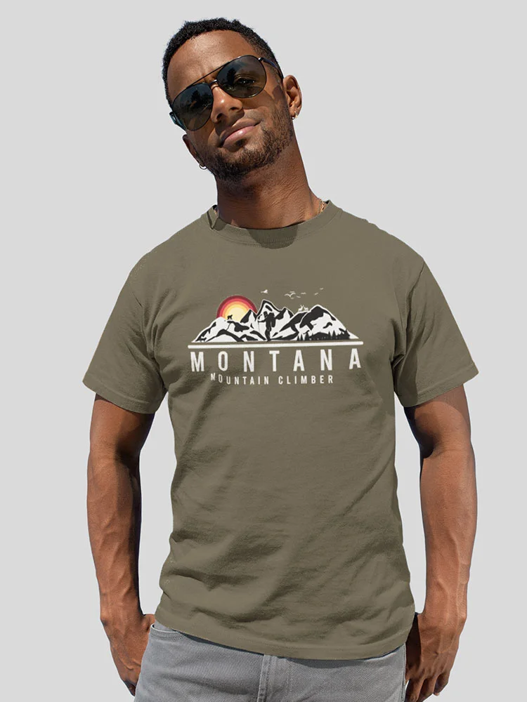 A person wearing sunglasses and an olive green t-shirt with "Montana Mountain Climber" print stands against a plain background, looking confident.