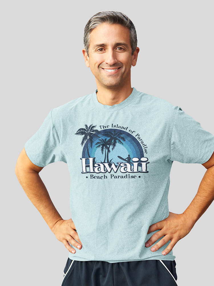 A person with short hair, smiling at the camera, wearing a Hawaii-themed t-shirt. Stands with one hand on hip against a gray background.