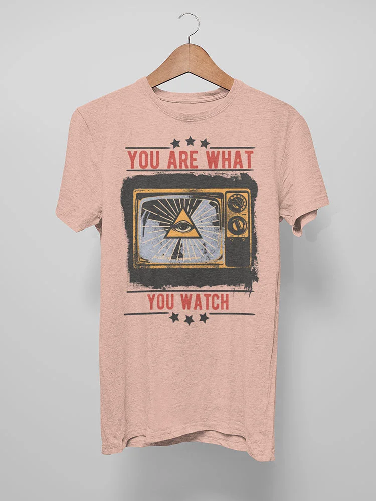 The image shows a salmon pink t-shirt with a vintage graphic design featuring the phrase "YOU ARE WHAT YOU WATCH" and an old television set.