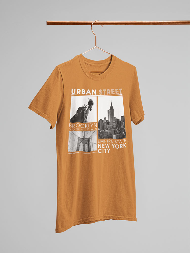 An orange t-shirt with "Urban Street" text and a New York City themed graphic hangs on a copper hanger against a neutral background.