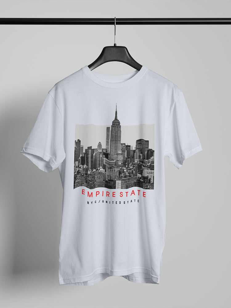 A white T-shirt with a black and white cityscape print, featuring the Empire State Building, hangs on a hanger against a plain background.