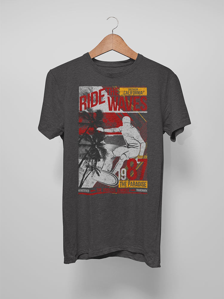 A gray t-shirt with a surf-themed graphic hangs on a hanger against a white background, featuring text "Ride the Waves," palm trees, and a surfer.