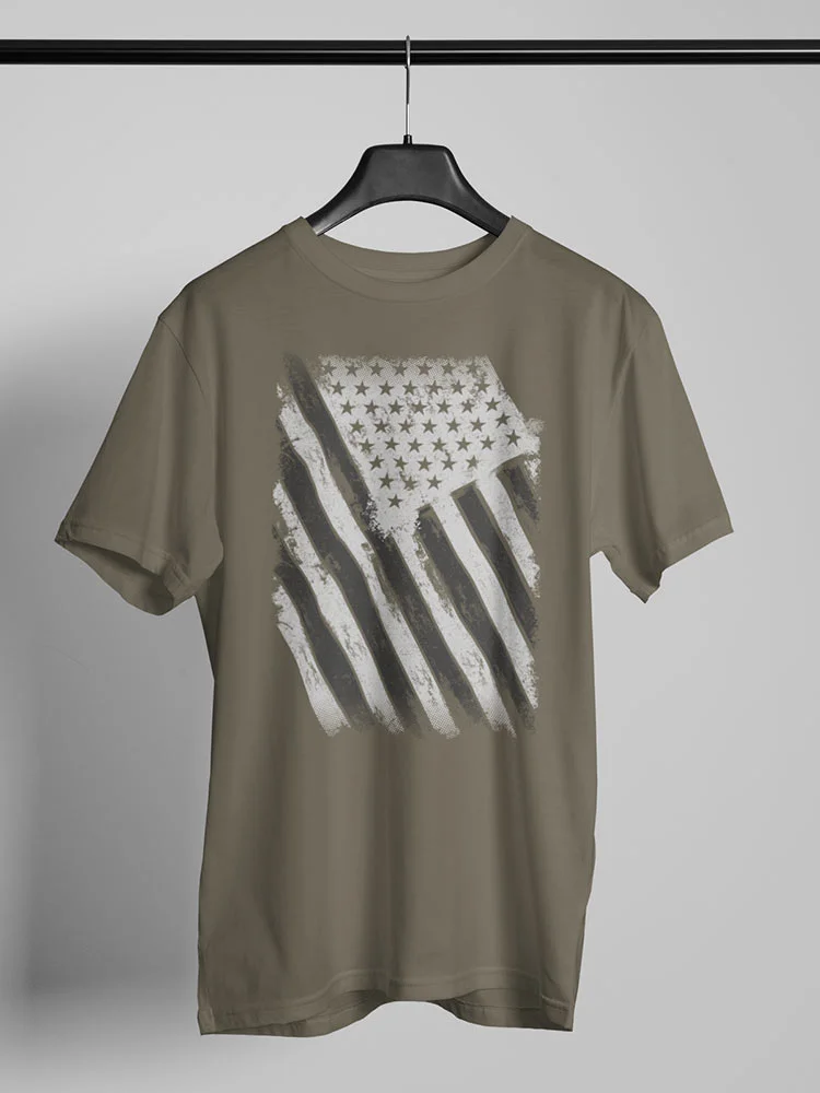An olive green t-shirt with a distressed American flag design hanging on a black hanger against a white background with a gray shadow below.