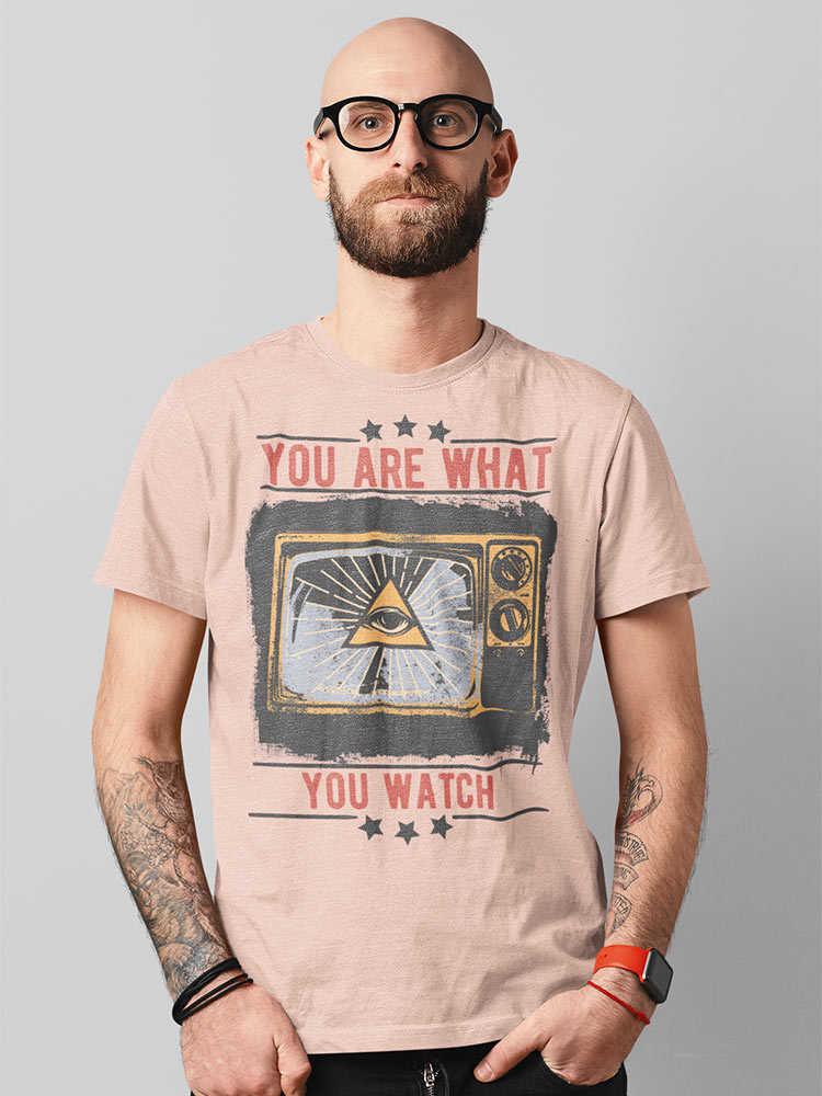 A bald person with a beard and glasses is wearing a graphic T-shirt with the phrase "YOU ARE WHAT YOU WATCH" and tattooed arms against a gray background.