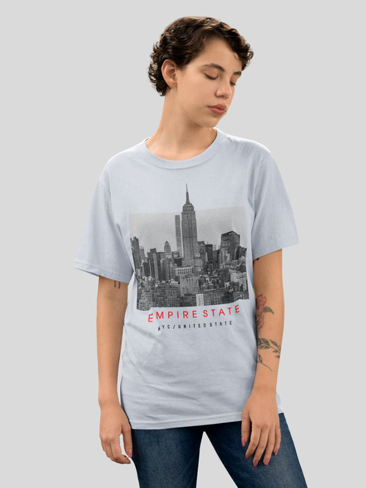 A person stands with closed eyes, wearing a light blue T-shirt featuring a black and white print of the Empire State Building and text.