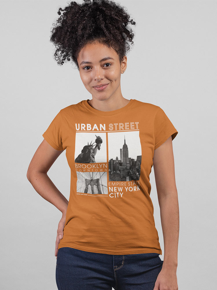 A person is wearing a mustard t-shirt with "Urban Street, Brooklyn Downtown, Empire State, New York City" graphics, paired with blue jeans, smiling gently.