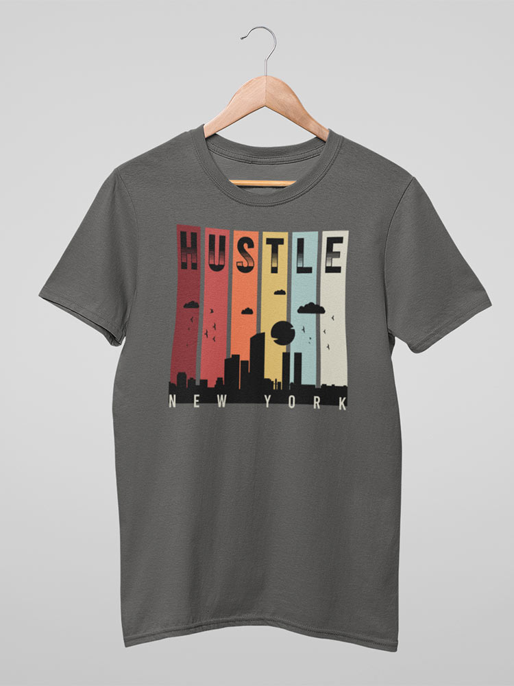 A gray t-shirt with a colorful "HUSTLE NEW YORK" cityscape graphic design hangs on a wooden hanger against a neutral background.
