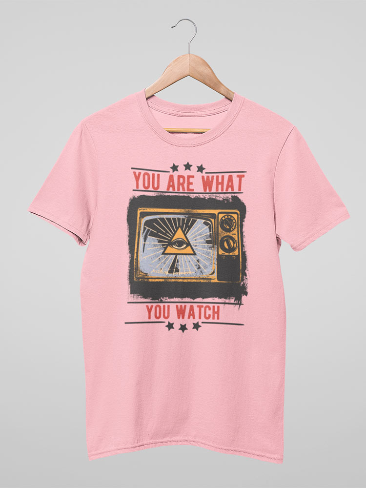 A pink t-shirt with a retro television graphic and text "YOU ARE WHAT YOU WATCH" hangs on a wooden hanger against a neutral background.