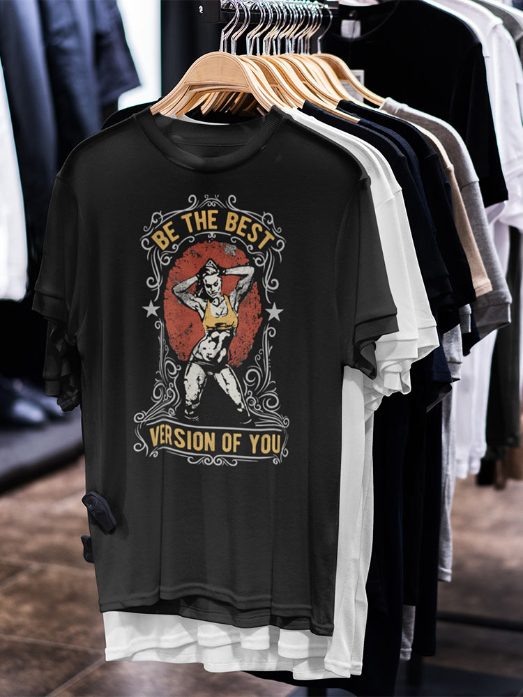 Black graphic t-shirt with motivational slogan and illustration hanging amongst other shirts on wooden hangers in a clothing store.