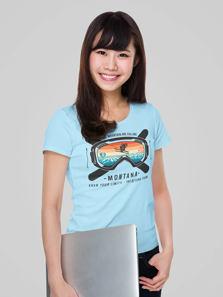 A smiling person is holding a laptop, wearing a blue t-shirt with a ski goggle graphic, against a light grey background.