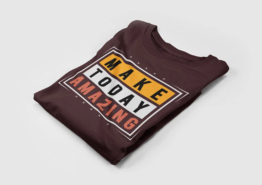Folded, maroon t-shirt with motivational message "MAKE TODAY AMAZING" in bold, colorful font against a white background on a flat surface.